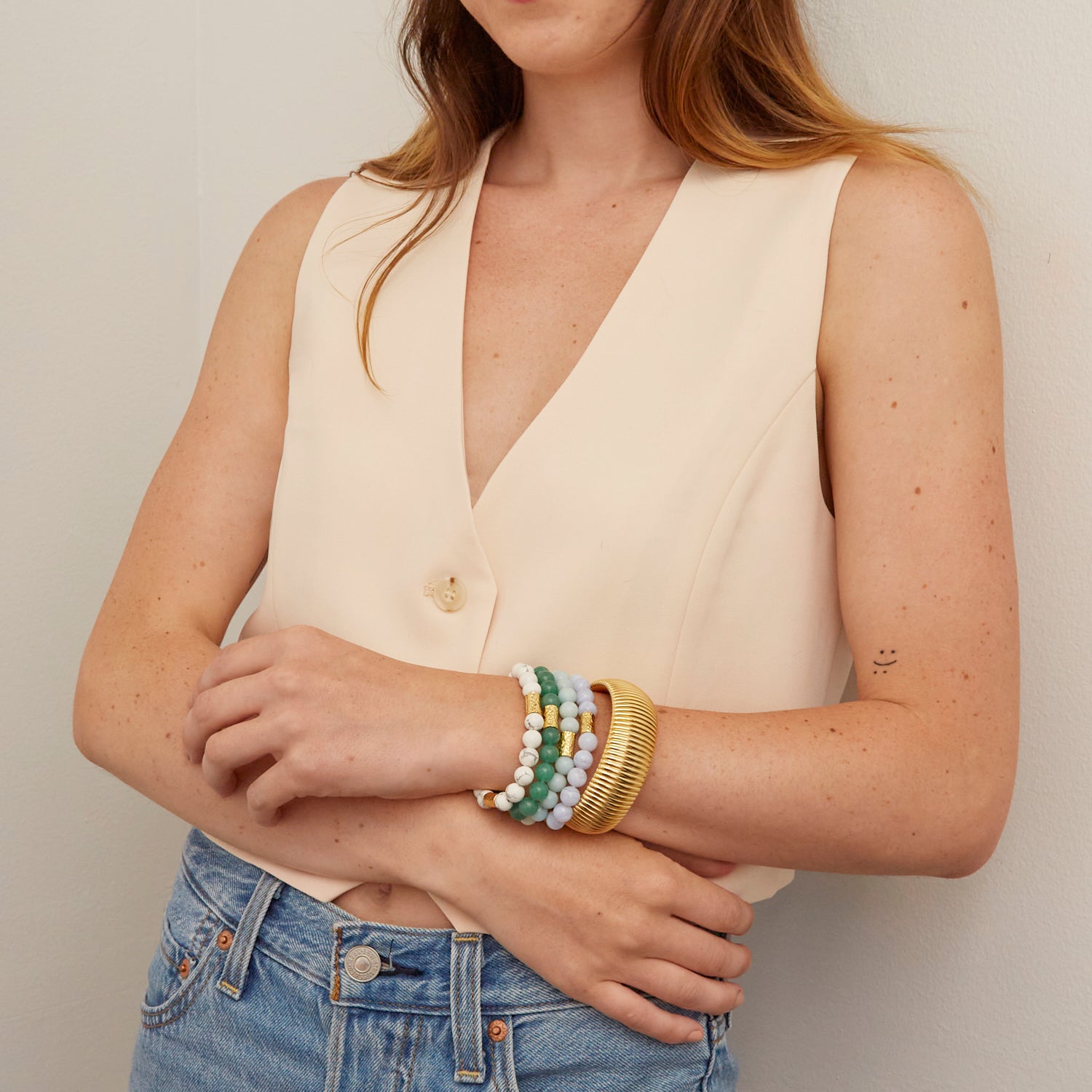 woman wearing large gold bangle and colorful beaded bracelets