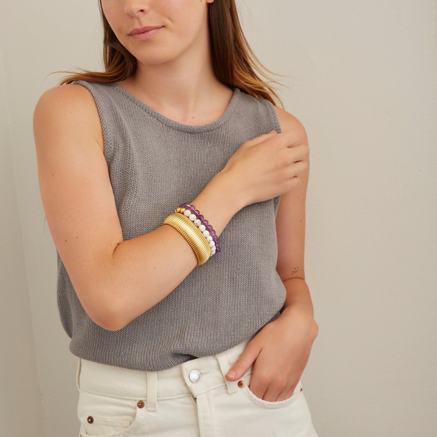 woman wearing large gold bangle and purple and white beaded bracelets