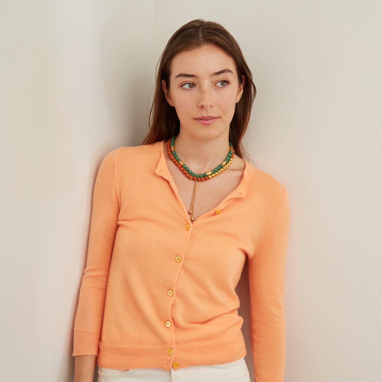 woman in orange cardigan wearing green and orange stone necklaces